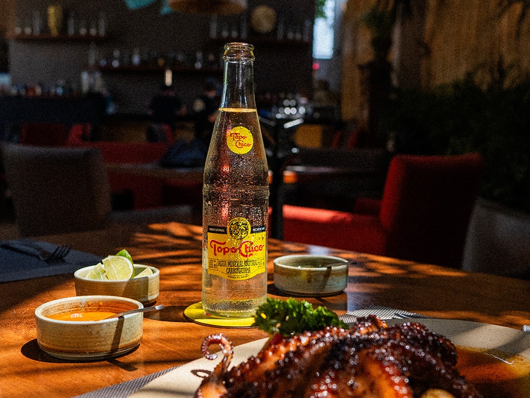 Botella de vidrio Topo Chico arriba de una mesa con comida.