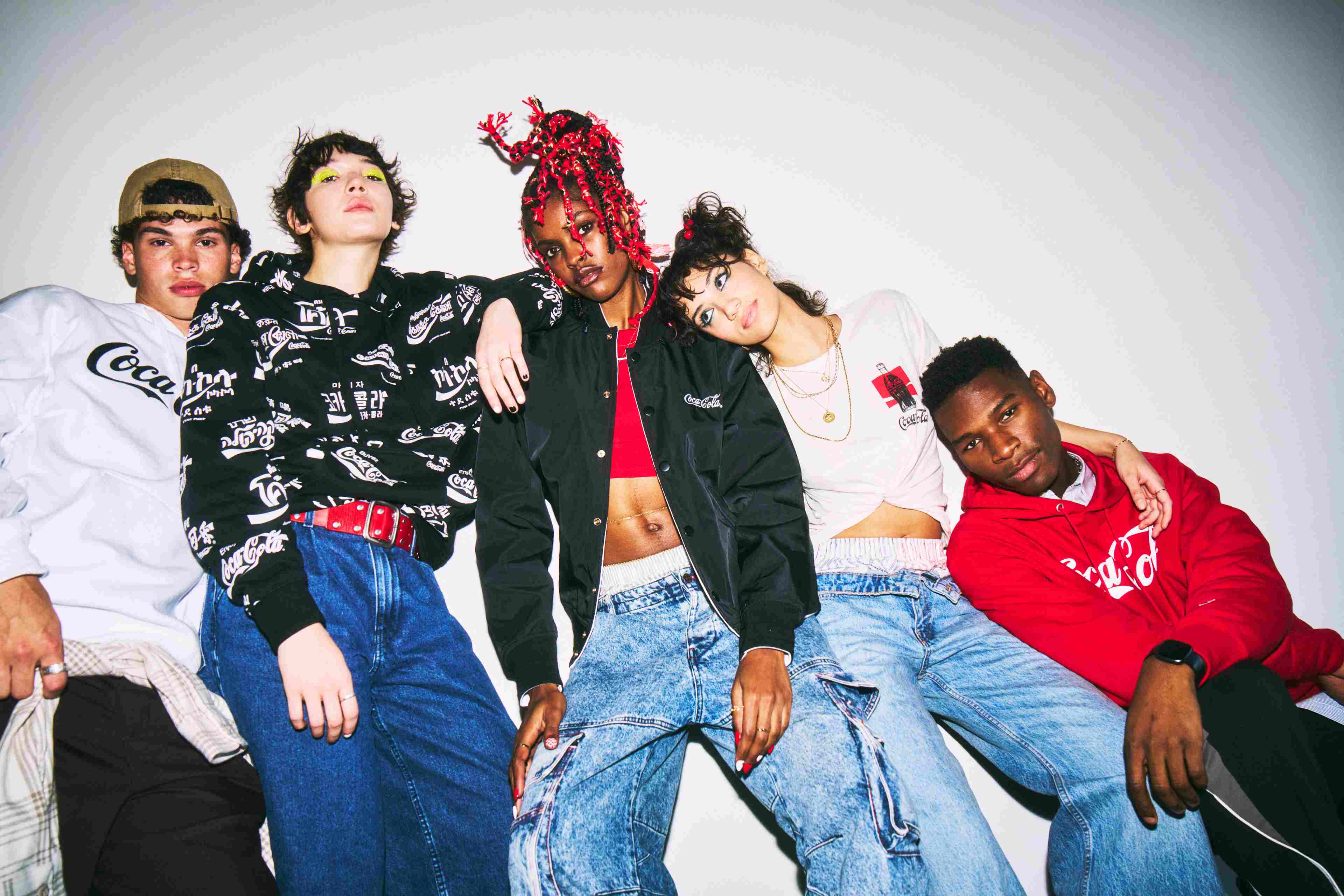 Grupo diverso de jóvenes posando juntos con ropa casual y prendas de Coca-Cola, en una sesión fotográfica de estilo urbano.