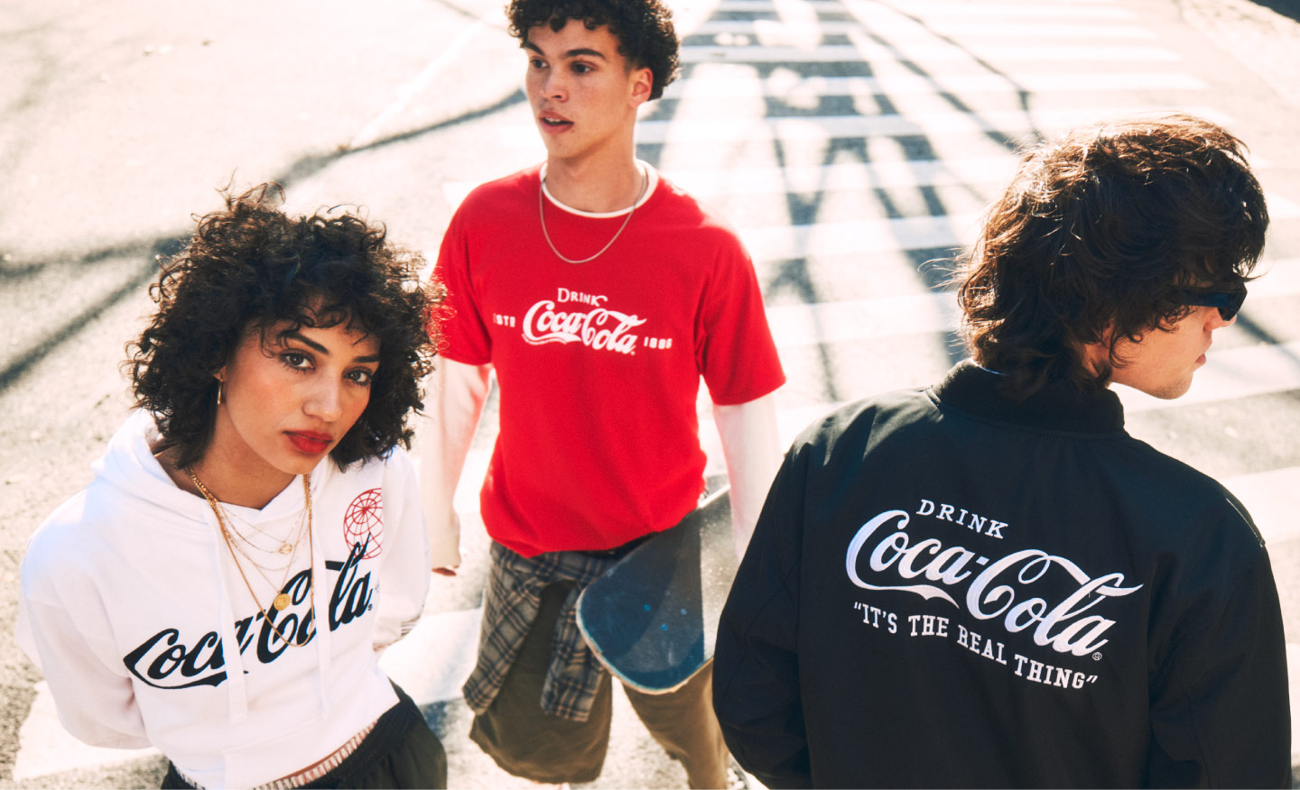 Grupo de jóvenes usando sudaderas y camisetas de Coca-Cola, reunidos al aire libre con patineta, en un ambiente urbano.​