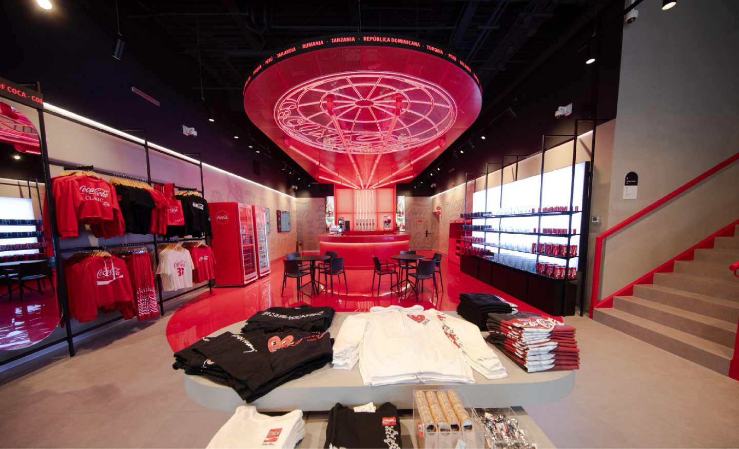 Interior de House of Coca-Cola con barra central, mesas para visitantes, iluminación roja y exhibición de productos de la marca.