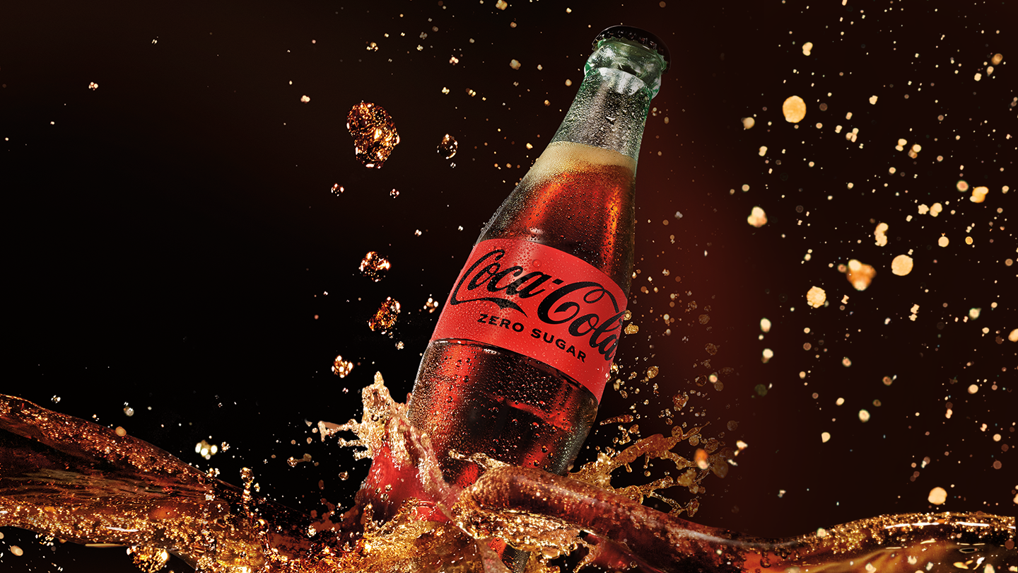 Staklena boca Coca-Cola Zero Sugar sa kapljicama i prskanjem pića na tamnoj pozadini