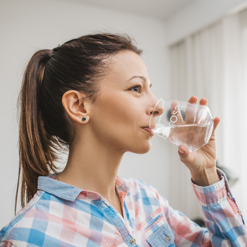 Osoba u košulji na kvadrate pije vodu iz čaše sa logotipom Rosa