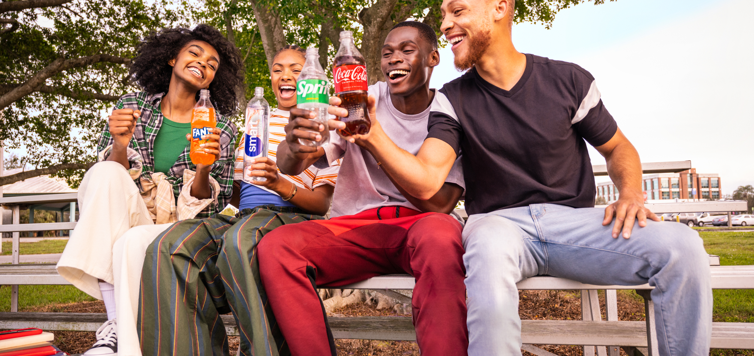 Friends sitting on a bench outside smiling and drinking Coca-Cola products