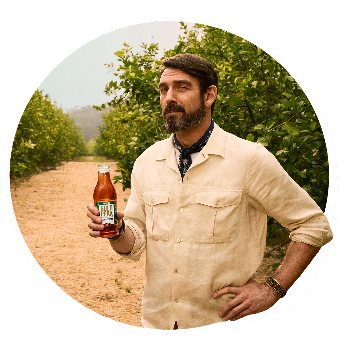 norm: a man with hand on hip holding a gold peak in front of greenery